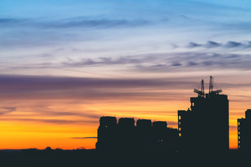 Obraz premium Cityscape with wonderful varicolored vivid dawn. Amazing dramatic blue sky with purple and violet clouds above dark silhouettes of city buildings. Atmospheric background of orange sunrise. Copy space.