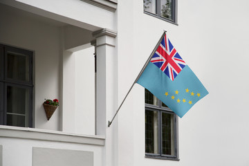 Tuvalu flag hanging on a pole in front of the house. National flag waving on a home displaying on a pole on a front door of a building and raised at a full staff.