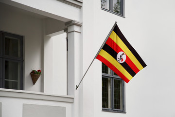 Uganda flag hanging on a pole in front of the house. National flag waving on a home displaying on a pole on a front door of a building and raised at a full staff.