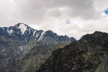 Fototapeta premium Snow on giant rocky ridge under cloudy sky. Atmospheric dark mountainside. Amazing snowy mountain range in overcast weather. Wonderful rocks. Wonderful shaded landscape of majestic nature of highlands