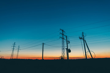 Power lines in field on sunrise background. Silhouettes of poles with wires at dawn. Cables of high...