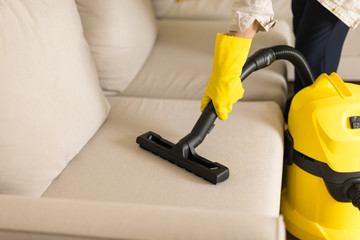 Woman cleaning sofa with yellow vacuum cleaner. Copy space. Clean concept