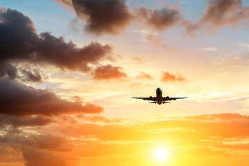 Commercial airplane flying above dramatic clouds during sunset