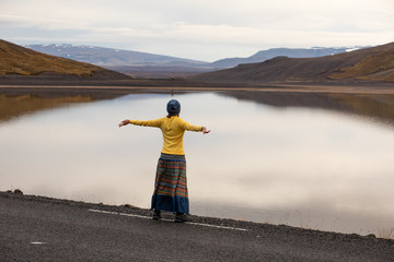 The girl in yellow admires the view of the river and the hill in the rays of the rising sun. Early morning day in Iceland. Car tourism in Iceland.