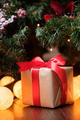 A gift in craft paper with a red ribbon on the background of a New Year's decorated Christmas tree with lights.