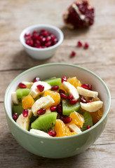 Salad of slices of various fruits and pomegranate seeds on a wooden background.