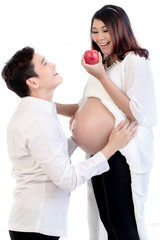 Happy pregnant wife holding an apple standing with his husband over white background