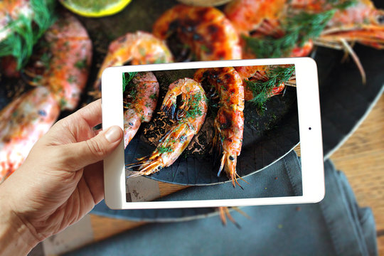closeup of hand holding holding tablet take photo of seafood on table
