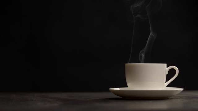 Slow motion shot of steaming cup of coffee over black background