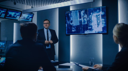 Special Agent in Charge Shows Satellite Surveillance Footage of the Car Getaway to a Team of Government Agents. GPS Tracking Fugitive in the Big Monitoring Room Full of Computers with Animated Screens