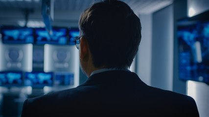 Back View Shot of the Government Official / Politician / Newsroom Reporter / Business Man Standing in the Room with Blurred Screens.