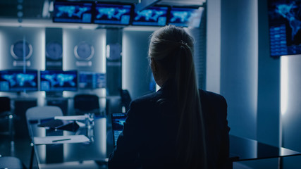 Female Special Agent Works on a Laptop in the Background Special Agent in Charge Talks To Military Man in Monitoring Room. In the Background Busy System Control Center with Monitors Showing Data Flow.