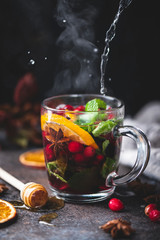 Hot fruit tea with spices, orange peel and mint. Steaming glass cup of hot tea, mulled wine with cranberries or spicy cranberry grog