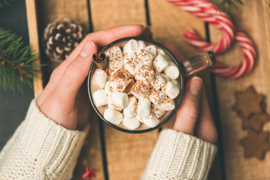 Cup of hot chocolate with marshmallows in girl hands. Female holding warm cozy comfort drink. Top view, toned image