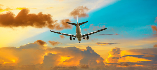 Airplane flying above dramatic clouds during sunset