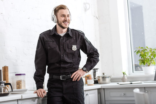 smiling police officer listening to music with headphones at kitchen