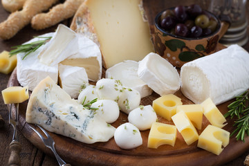 Cheese platter with a variety of types of cheese - gorgonzola, mozzarella, , camembert, toma, emmental and fresh caprino - served on rustic wood with olives and breadsticks