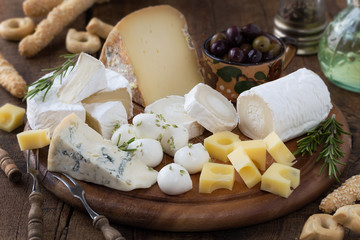 Cheese platter with a variety of types of cheese - gorgonzola, mozzarella, , camembert, toma, emmental and fresh caprino - served on rustic wood with olives and breadsticks