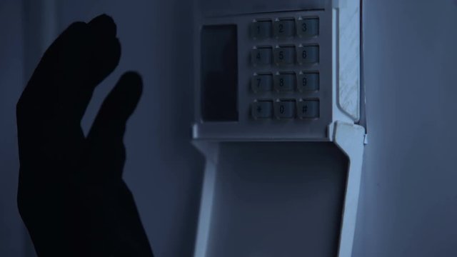 Thiefs hand in glove unblocking security alarm system, bank robbery, close up