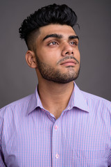 Young handsome Indian businessman against gray background