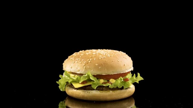 Rotation of delicious burger over black background. loop video, 4K