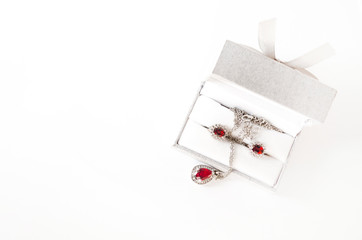 Jewelry set with red gems in the box, top view. Silver necklace and earrings with ruby gem. Gift,...