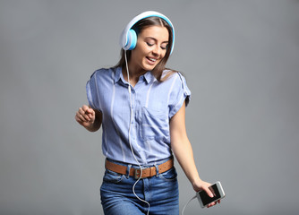 Beautiful woman listening to music on grey background