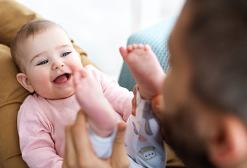 Unrecognizable father playing with baby daughter sitting indoors, having fun.