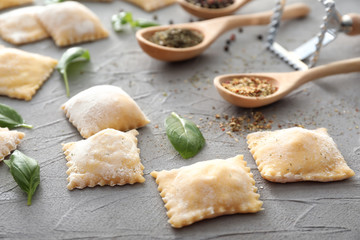 Uncooked ravioli with spices on grey textured background
