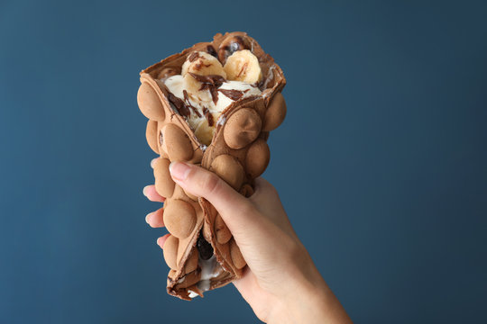 Female hand with delicious sweet bubble waffle on color background