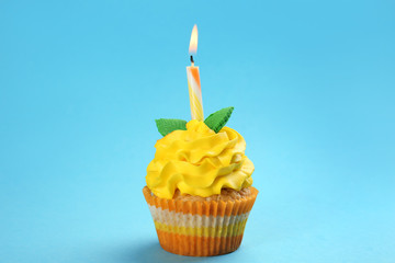 Tasty birthday cupcake with burning candle on color background