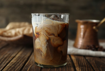 Glass of cold coffee with milk on wooden table