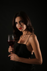 Beautiful young woman with glass of wine on dark background