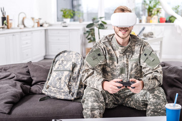 Fototapeta premium smiling army soldier in virtual reality headset playing video game on couch
