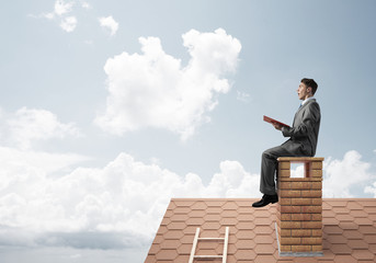 Student guy in suit on brick house roof reading book