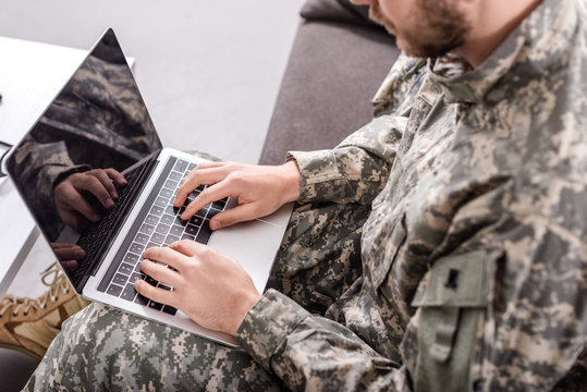 Partial view of army soldier using laptop on couch
