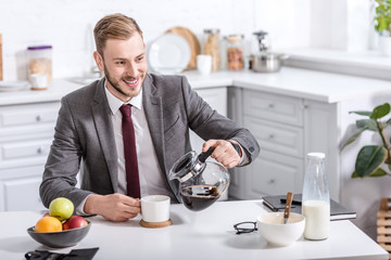 handsome businessman pouring filtered coffee in cup at kitchen table