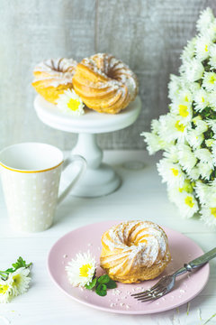 Delicious cake with coconut chips on pink plate on white table, autumn white chrysanthemum and cup of coffee