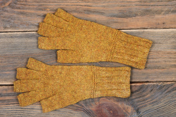 Yellow knitted gloves with open fingers on a wooden background. Handwork. View from above.