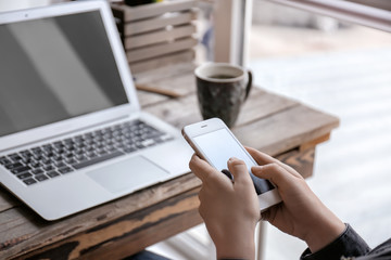 Woman with mobile phone and laptop sitting at table, closeup