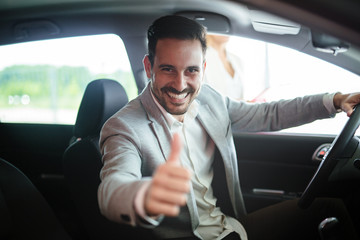 Portrait of handsome young man taking luxury car for test drive, sitting inside and smiling