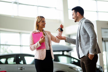 Professional salesperson during work with customer at car dealership. Giving keys to new car owner.