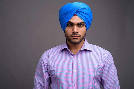 Young handsome Indian businessman wearing turban against gray ba - Powered by Adobe