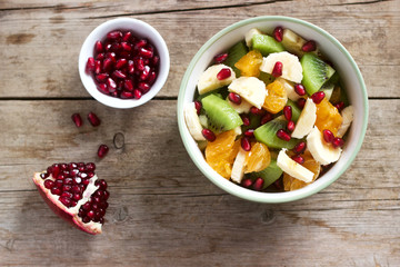 Salad of slices of various fruits and pomegranate seeds on a wooden background.