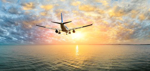 Airplane flying over the sea at sunset