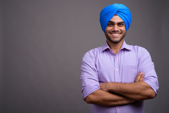 Young handsome Indian businessman wearing turban against gray ba - Powered by Adobe