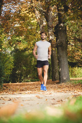 Closeup of one young athlete man running on a path in the park during autumn.