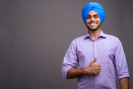Young handsome Indian businessman wearing turban against gray ba - Powered by Adobe