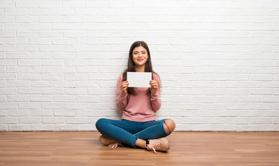 Teenager girl sitting on the floor in a room holding a placard for insert a concept