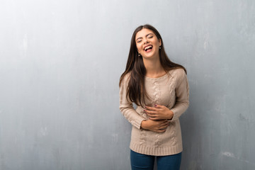 Teenager girl with sweater on a vintage wall smiling a lot while putting hands on chest